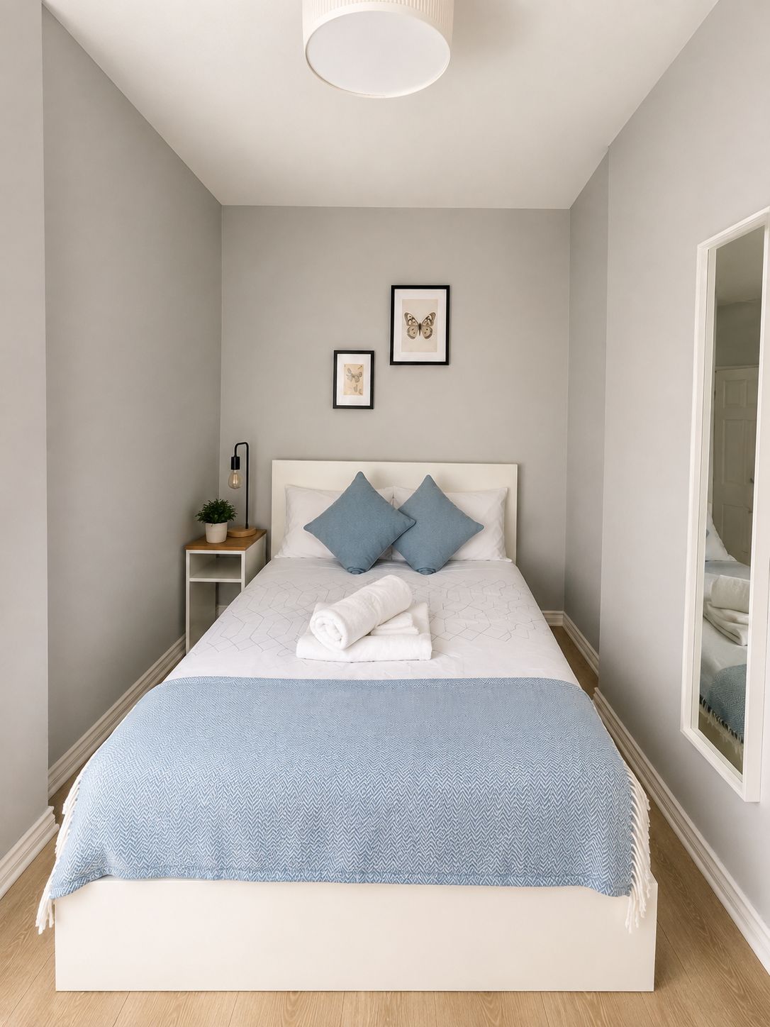 A neatly made bed with a blue blanket, a bedside lamp, and two framed pictures on the wall.