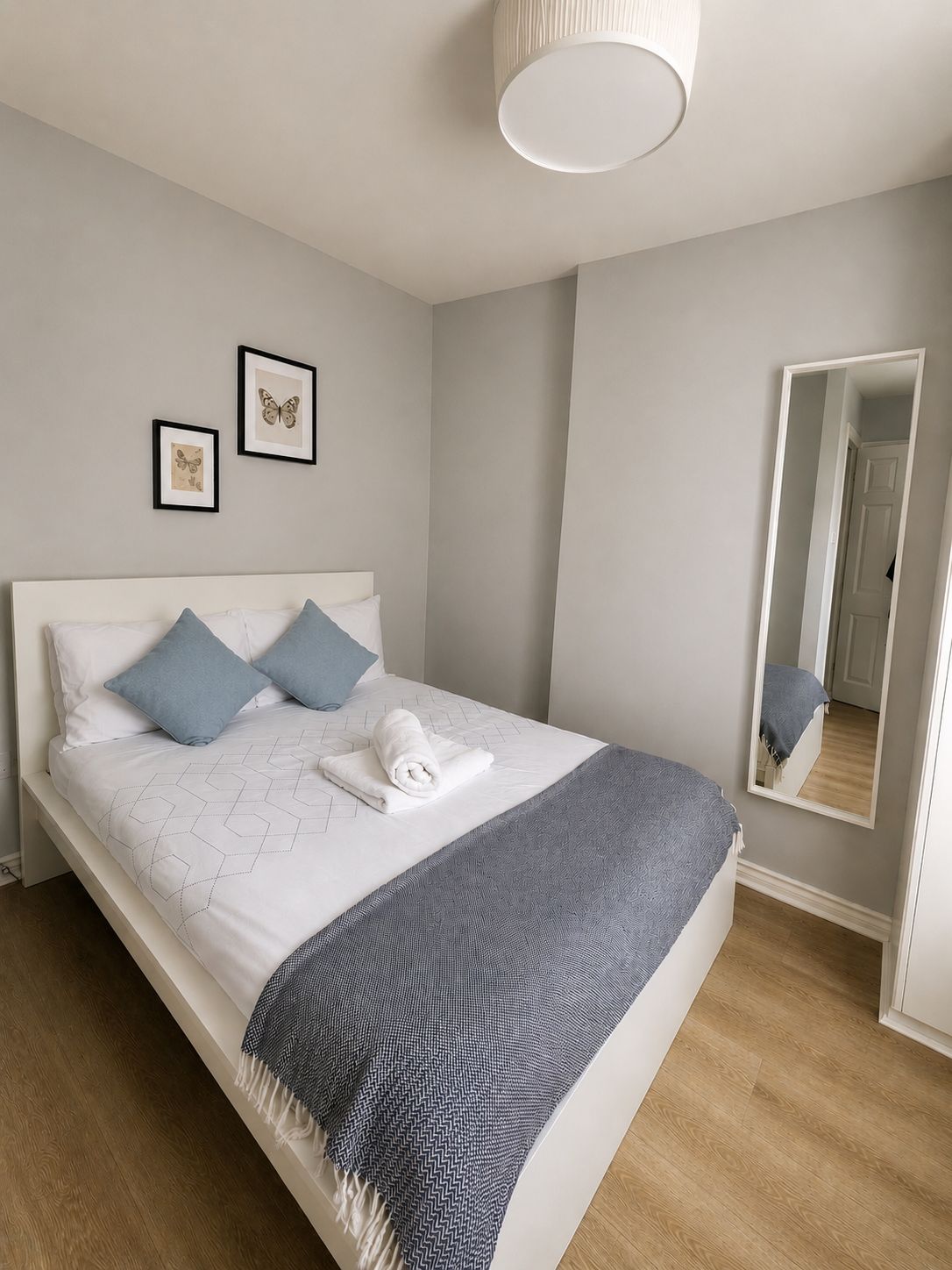 A neatly made bed with a white headboard, a grey blanket, and two blue pillows.