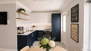 A modern kitchen with white and navy blue cabinets, a coffee machine, and a dining table with a vase of flowers.