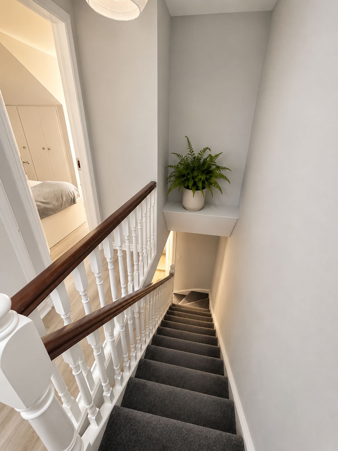 A staircase with a wooden handrail, carpeted steps, and a potted plant on a shelf.
