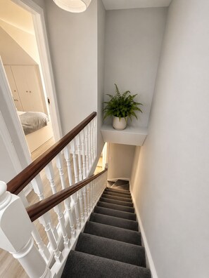 Eine Treppe mit Holzgeländer, Teppichstufen und einem Blumentopf auf einem Regal.