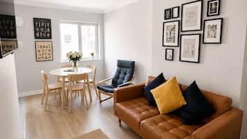 A modern living room with a brown leather sofa, a dining table with chairs, and a large window.
