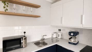A modern kitchen with white cabinets, a black microwave, a coffee maker, and a sink.