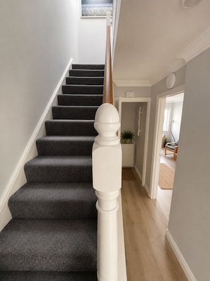 Una escalera con peldaños cubiertos de alfombra oscura y barandilla blanca.