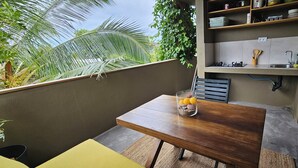 A balcony with a wooden table, a glass container with oranges, and a kitchen area with shelves and utensils. - Mapou Studio Apartment with Pool 15min from Grand Bay (Mauritius)