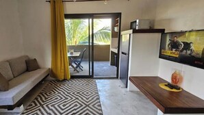 A compact living space with a sofa, a coffee table, a TV, and a sliding door leading to an outdoor area with a table and chairs. - Mapou Studio Apartment with Pool 15min from Grand Bay (Mauritius)