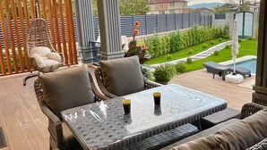 Une terrasse extérieure aménagée avec des meubles en osier, une table en verre et une vue sur un jardin et une piscine.