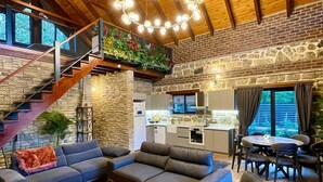 Un vaste espace de vie doté d’un haut plafond en bois, d’un mur en pierre, d’un escalier, d’une cuisine et d’un coin repas.