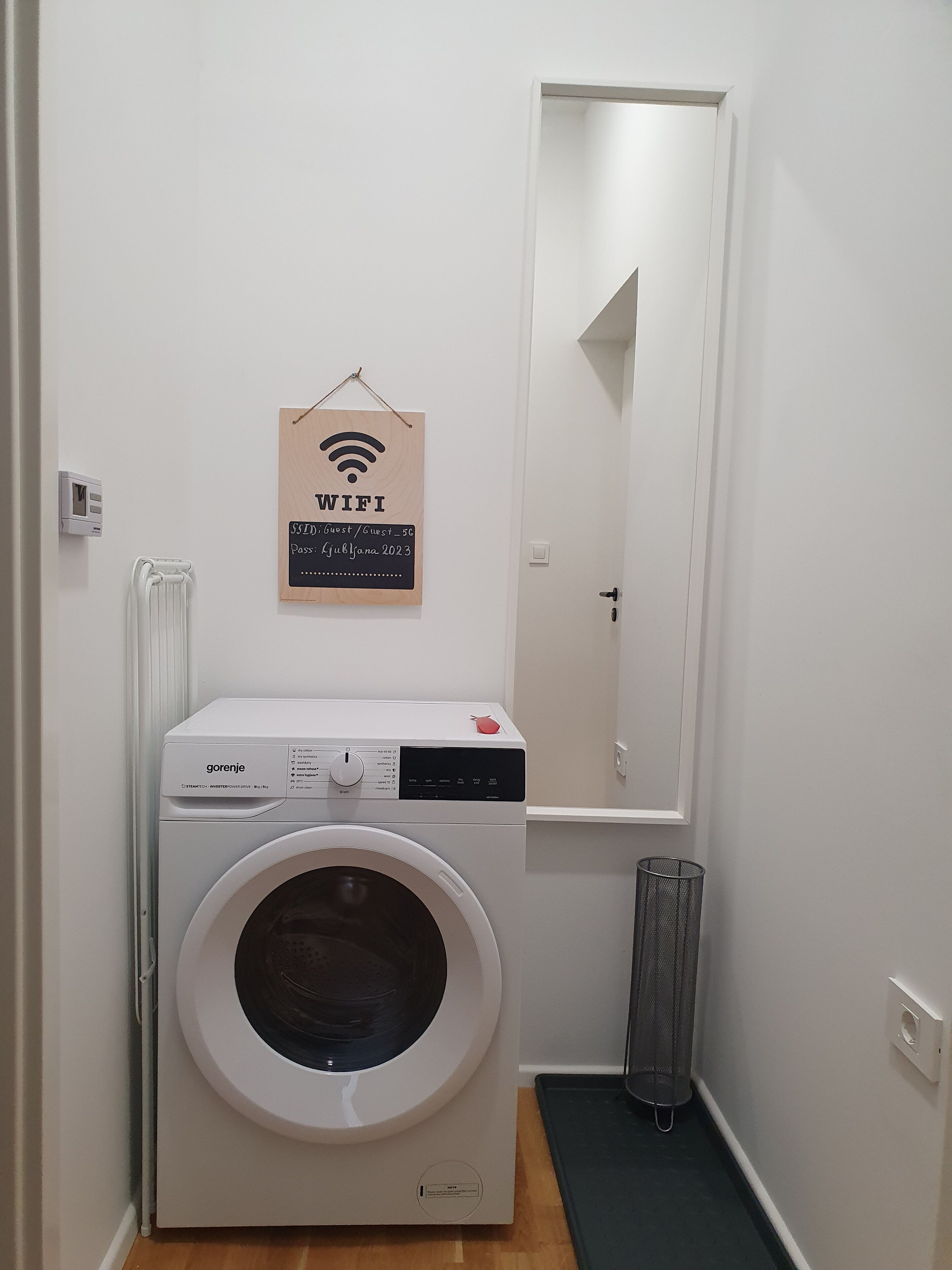 A laundry room with a white washing machine, a WiFi sign, and a mirror.