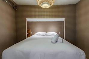 A hotel room with a large bed, a ceiling light fixture, and a wardrobe.