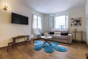 Ein Wohnzimmer mit Sofa, Fernseher, Tisch, Couchtisch, Teppich und Wandlampe.
