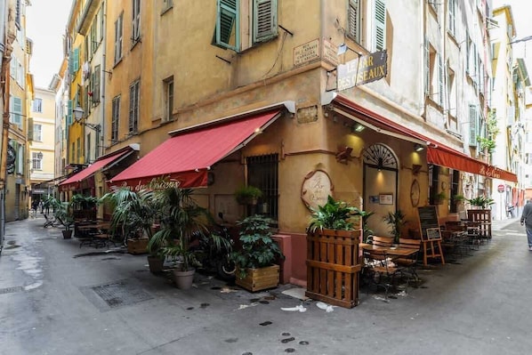 Eine schmale Straße mit Außenplätzen, Topfpflanzen und einem Café mit roter Markise.