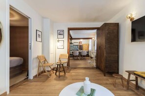 A room with a bed, a dining area with chairs and a table, and a TV mounted on the wall.