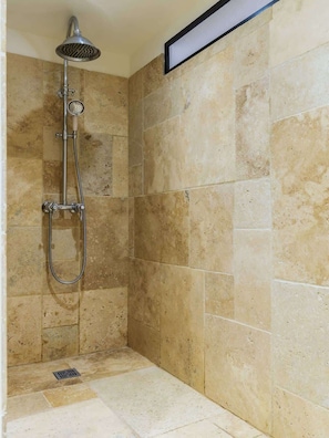 A shower area with a handheld showerhead, a wall-mounted showerhead, and a floor drain.
