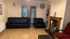 Un salon avec un canapé en cuir noir, un fauteuil rouge, une table basse en bois, une cheminée et une bibliothèque.