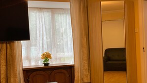 Une pièce avec une table en bois, un téléviseur fixé au mur, une fenêtre avec des rideaux légers et une porte coulissante donnant sur une autre pièce.