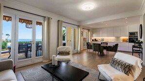 Amplia sala de estar con sofá, una mesa de centro y vista al océano a través de puertas correderas grandes.