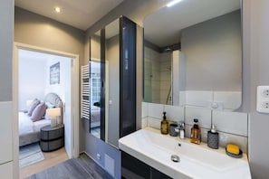 A modern bathroom with a large mirror, white sink, and toiletries.