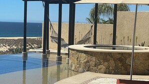A swimming pool with a stone surround, a hot tub, and a view of the ocean.