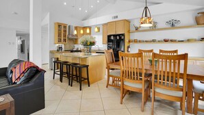 A modern kitchen with wooden cabinets, a central island, bar stools, and a dining table with chairs. - Casa Chiquita: HUGE Backyard, Heated Pool & Spa (Palm Springs)