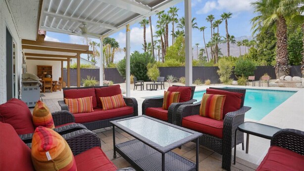 A covered outdoor patio with wicker furniture, a pool, and palm trees. - Casa Chiquita: HUGE Backyard, Heated Pool & Spa (Palm Springs)
