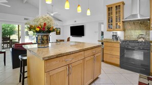 A modern kitchen with granite countertops, wooden cabinets, a stainless steel stove, and pendant lighting. - Casa Chiquita: HUGE Backyard, Heated Pool & Spa (Palm Springs)