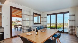Uma área de refeições moderna com mesa de madeira, cadeiras pretas e vista para o exterior.