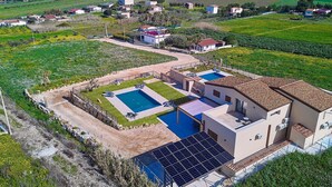 Uma vila moderna com duas piscinas, painel solar e vista para o campo circundante.