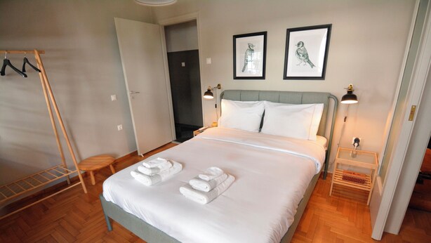 A neatly made bed with white linens and towels, a wooden floor, and two framed pictures on the wall. - Bibelot Acropolis (Athens)