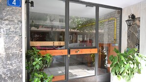 A hotel entrance with a glass door, a wooden bench outside, and potted plants. - Bibelot Acropolis (Athens)