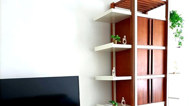 Een moderne woonkamer met een flatscreen televisie op een witte kast, houten planken met decoratieve objecten en vloertegels met een patroon.