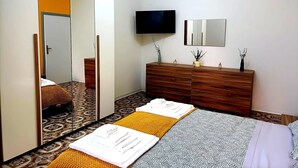 Een slaapkamer met een bed, een dressoir, een televisie, een spiegel en een deur.