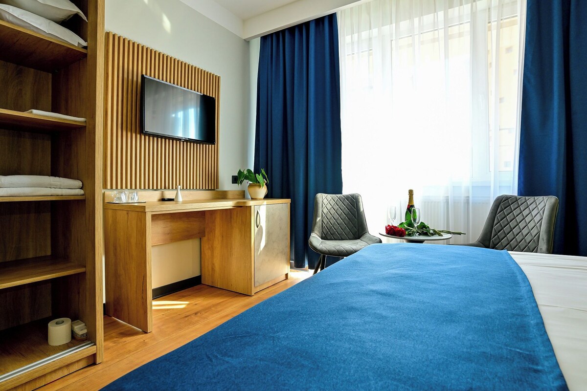 A hotel room with a bed, a desk, a TV, and a dining area with a table set for two.