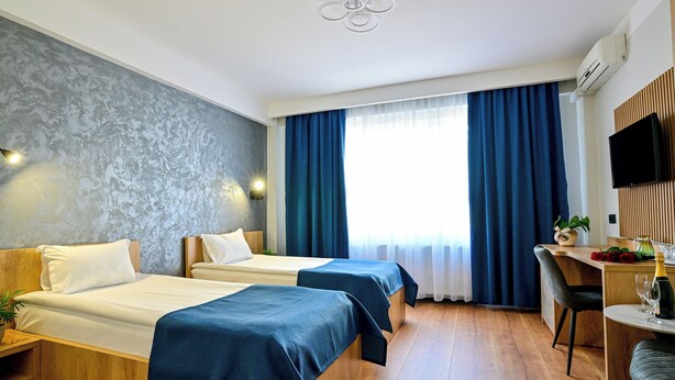 A hotel room with two beds, a desk with a chair, a television, and a window with curtains. - Hotel Class Sibiu (Sibiu)
