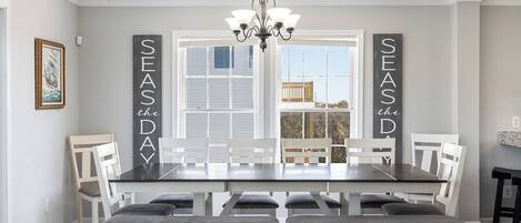 A dining area with a large table and white chairs, a chandelier, and two vertical banners reading "SEASONS the DAY".