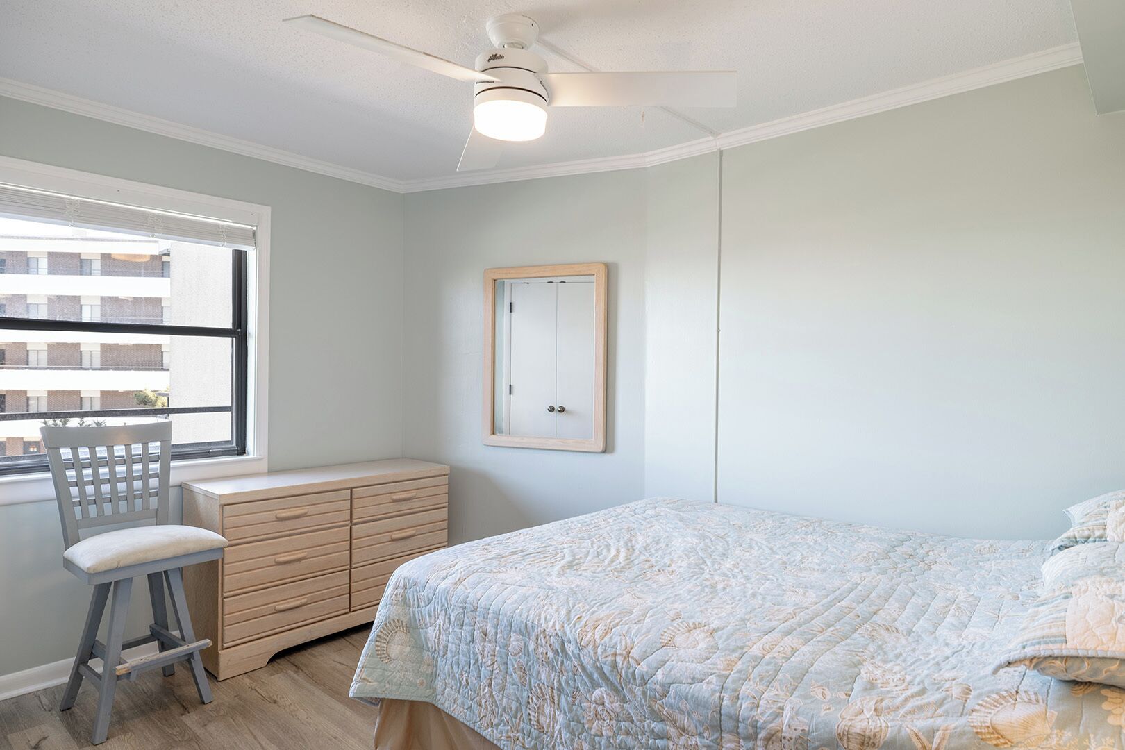 A bedroom with a bed, a dresser, a chair, a window, and a ceiling fan.