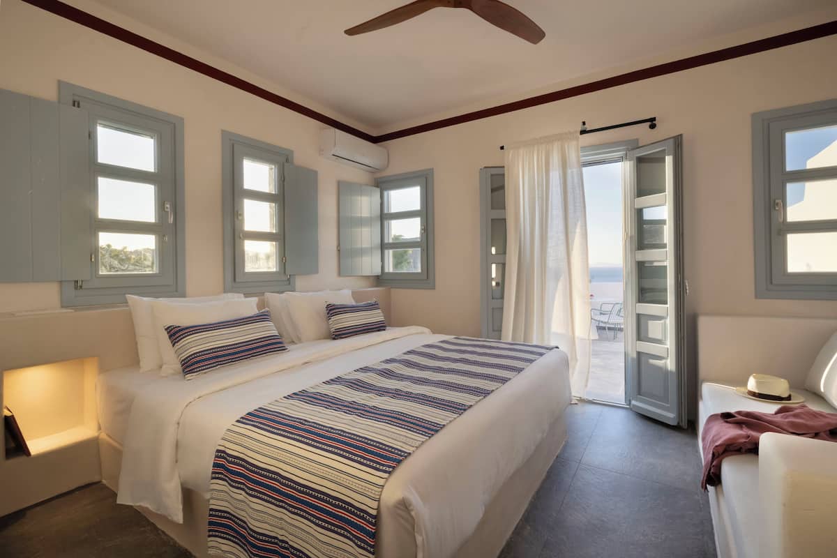 Een slaapkamer met een bed, nachtkastje, raam met gordijnen en een deur naar een balkon.