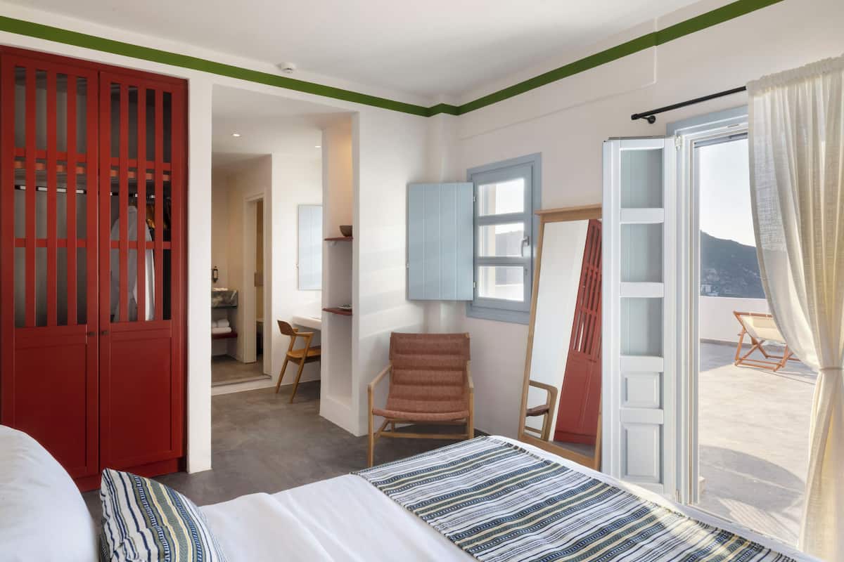 Een slaapkamer met een bed, een rode garderobe, een stoel, een bureau en uitzicht op het omliggende landschap.