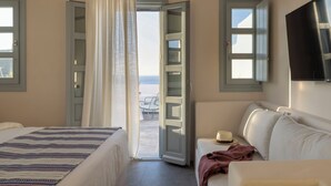 Een hotelkamer met een bed, een bank, een televisie en uitzicht op het strand door een open deur.