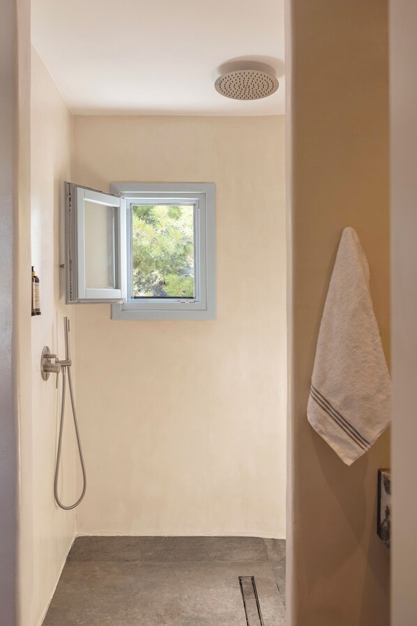 A bathroom with a shower, a towel hanging on the wall, and a window with a view of greenery.