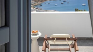 Een balkon met uitzicht op zee, een witte bijzettafel en een houten stoel.