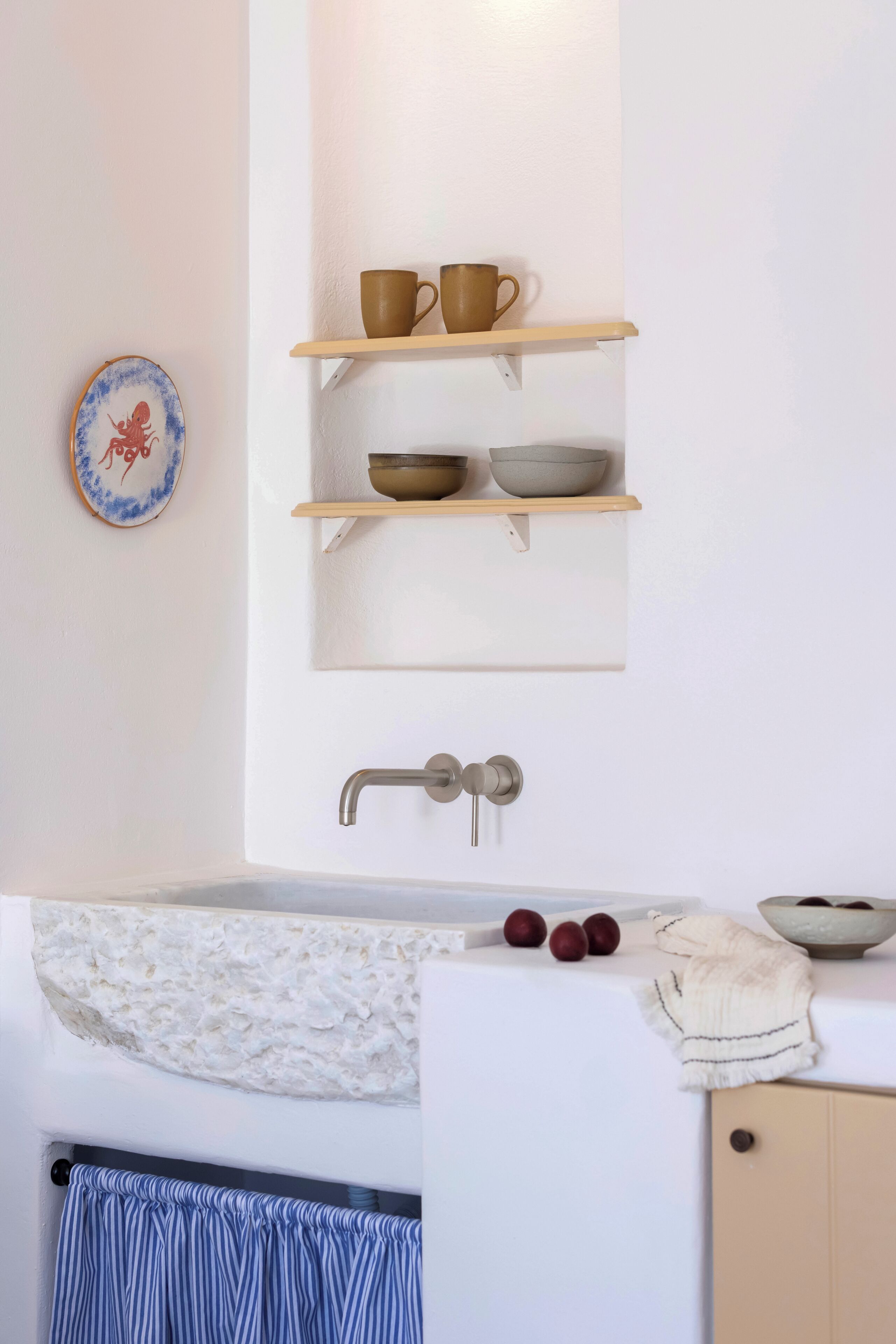Een badkamer met een witte wastafel, twee planken met bekers en kommen, een decoratief bord en een handdoekrek.