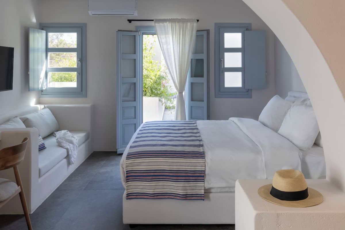 Een slaapkamer met een bed, een stoel, een hoed en uitzicht op het buiten.