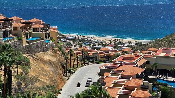 A coastal resort with multiple buildings, a swimming pool, and a road leading to the beach.