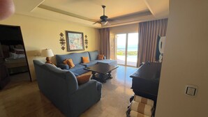 A living room with a sofa, a coffee table, and a TV. There is a balcony with a view of the ocean.