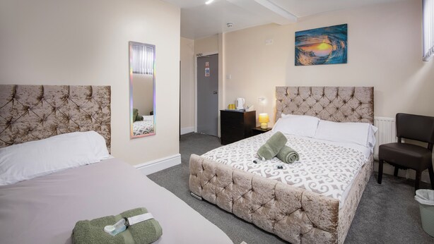 A hotel room with two beds, a chair, a desk, and a painting on the wall. - The Ocean Inn (Blackpool)