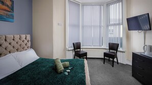 A hotel room with a bed, two chairs, a TV, and a window with blinds. - The Ocean Inn (Blackpool)