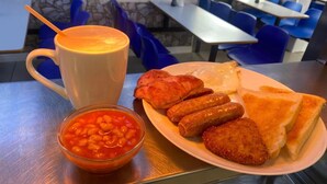 A meal consisting of toast, sausages, and baked beans on a plate, accompanied by a mug of coffee, all placed on a table. - The Ocean Inn (Blackpool)