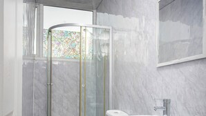 A modern bathroom with a shower, toilet, and sink, featuring marble walls and wooden flooring. - The Ocean Inn (Blackpool)