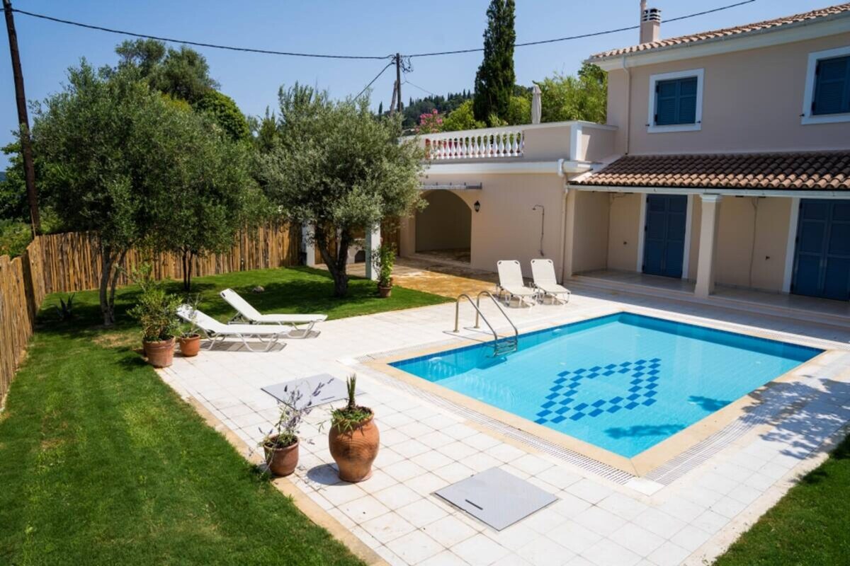 A swimming pool with a geometric pattern, surrounded by a tiled deck, potted plants, and lounge chairs.